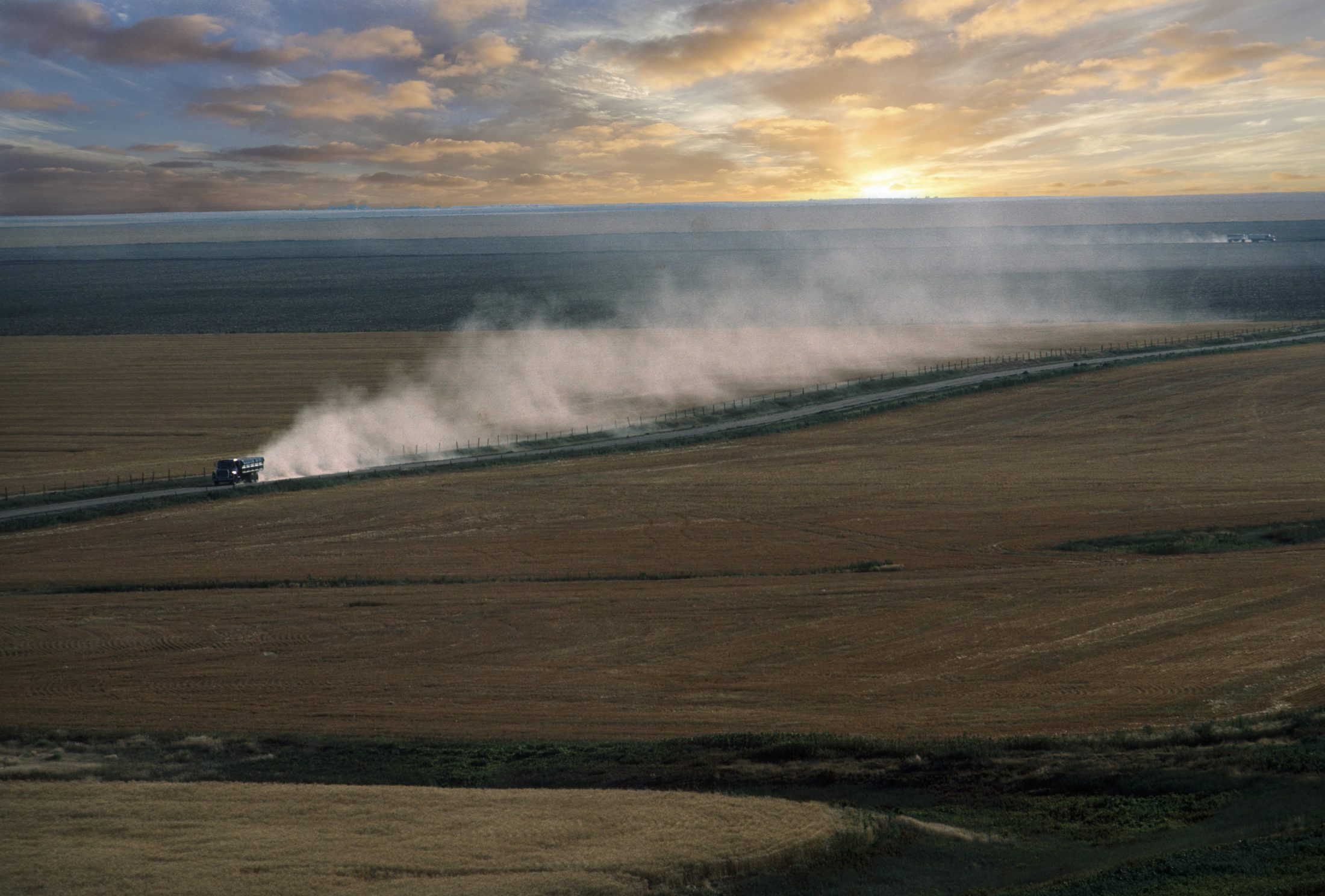 Wheat field at sunset, truck kicking up dust along a dirt road
