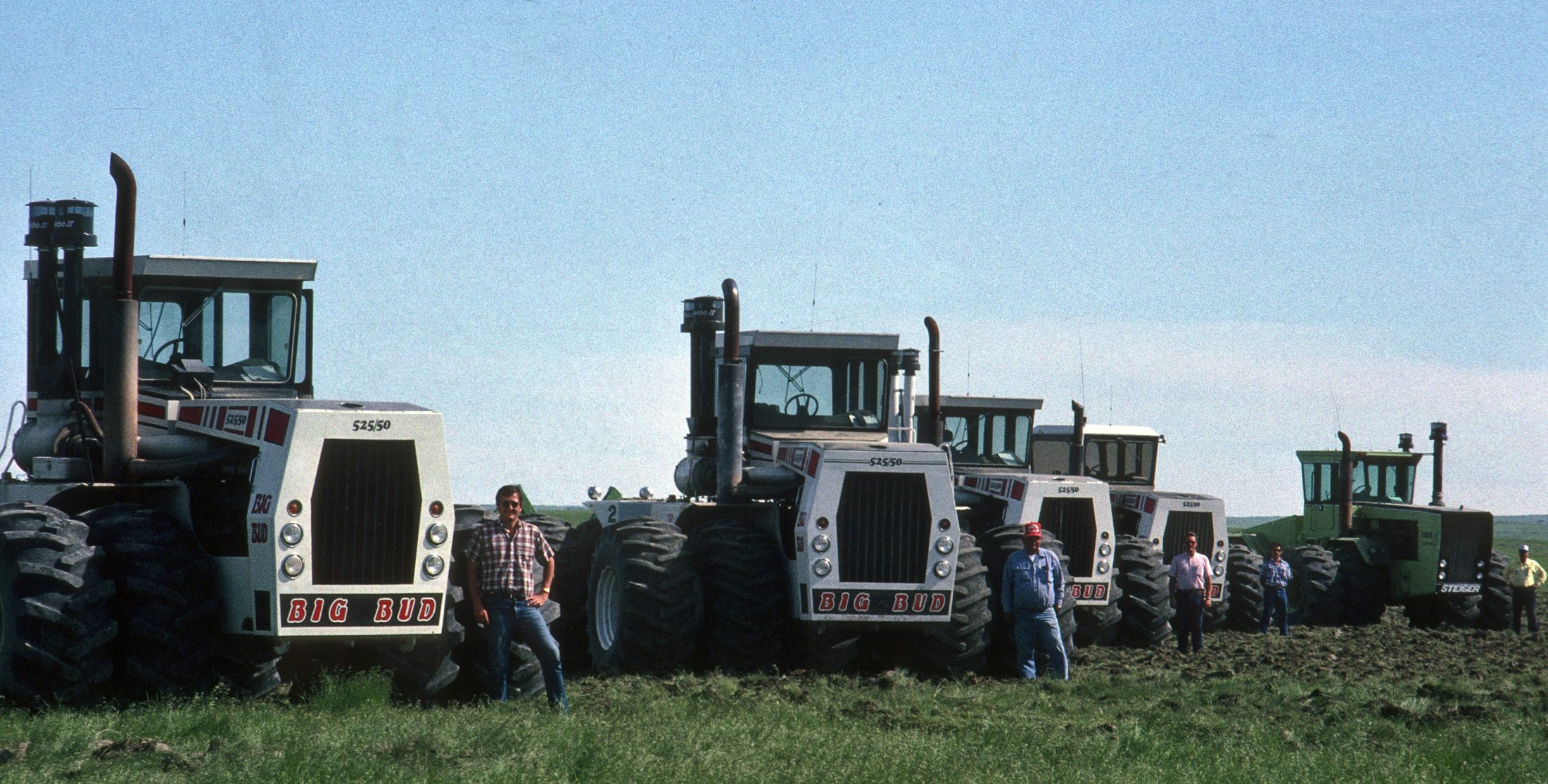 Lineup of Big Bud and Steiger tractors in a field, vintage photo