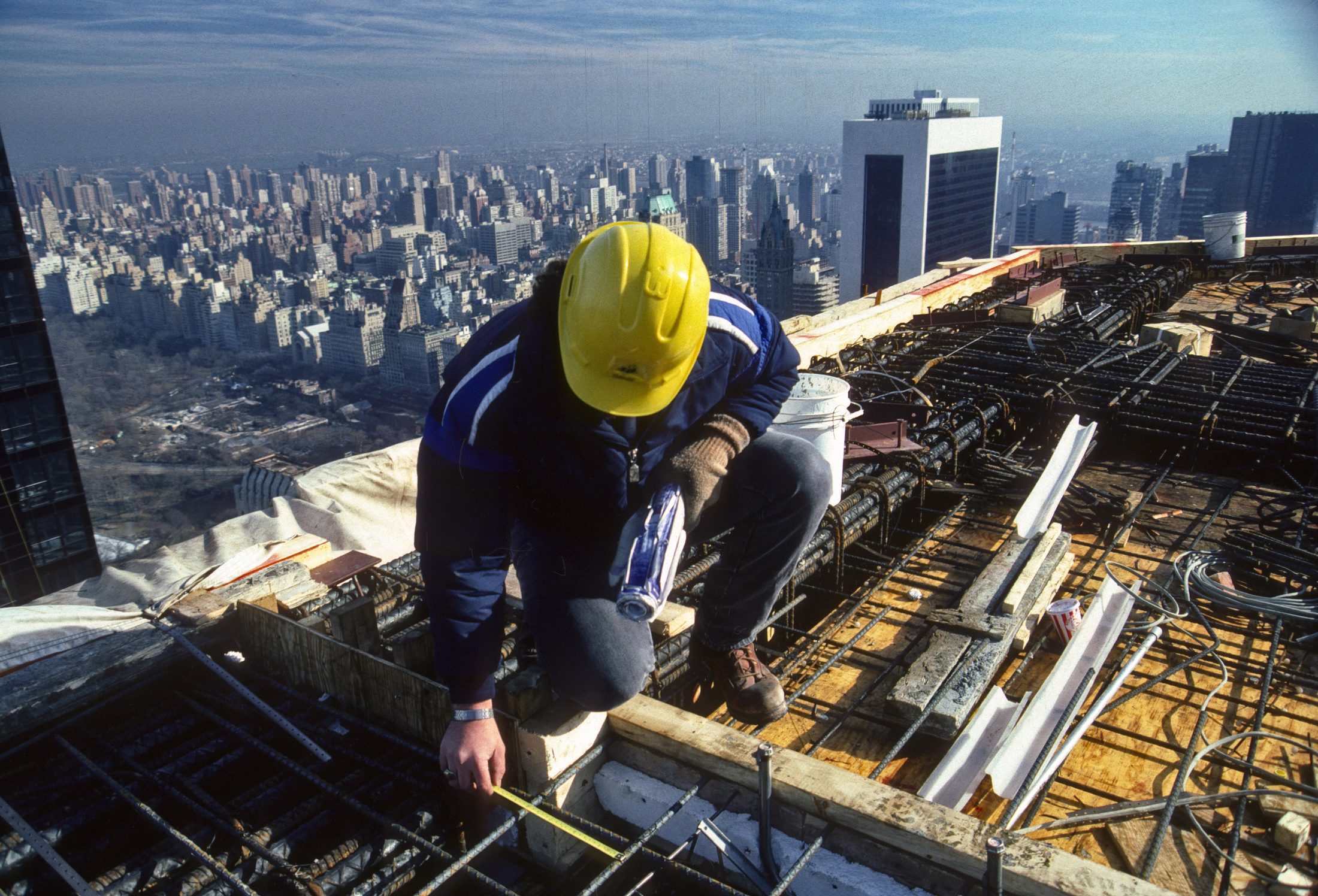 Construction worker measuring rebar, high above the city skyline