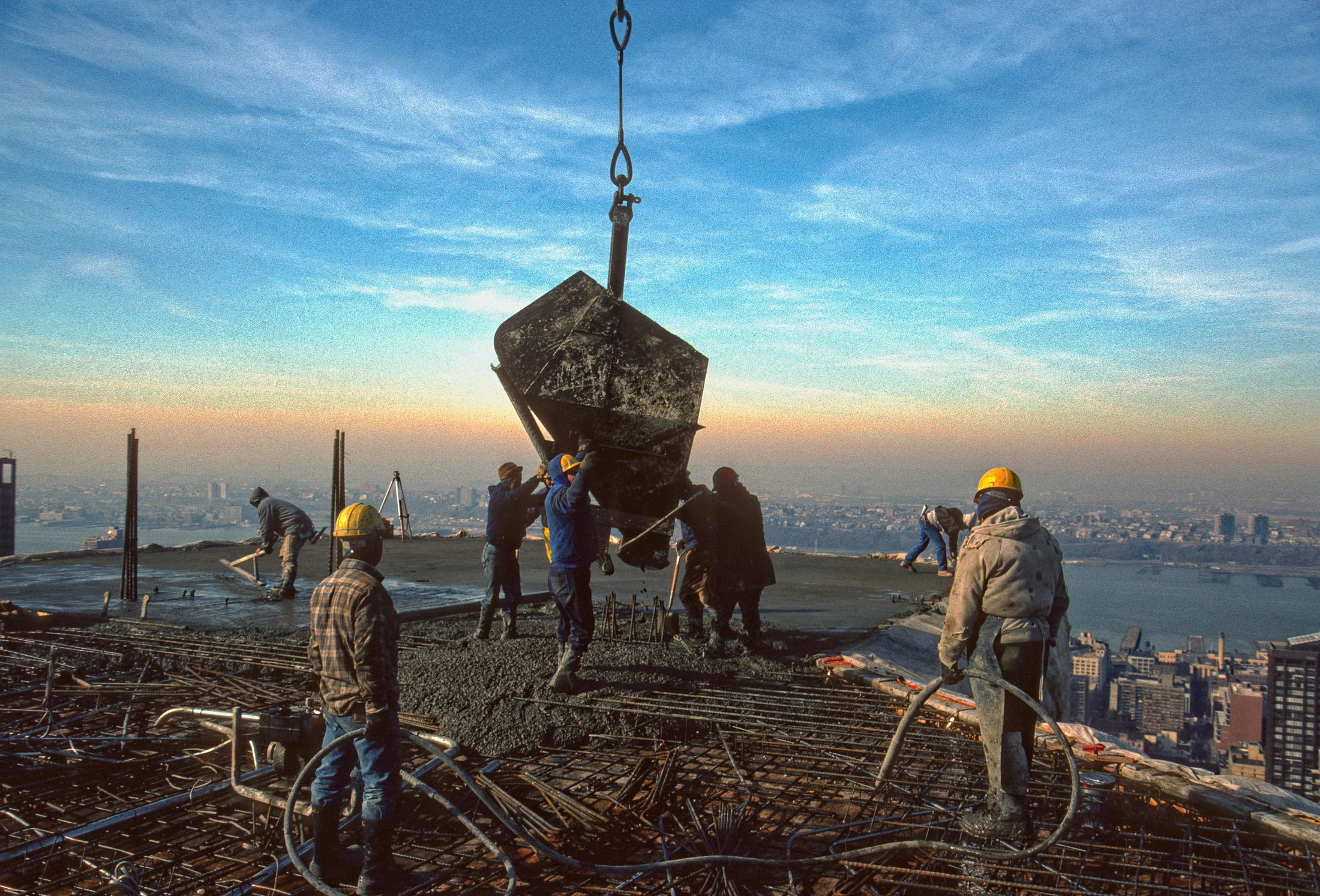 Crane lowering a concrete bucket to workers on a high-rise