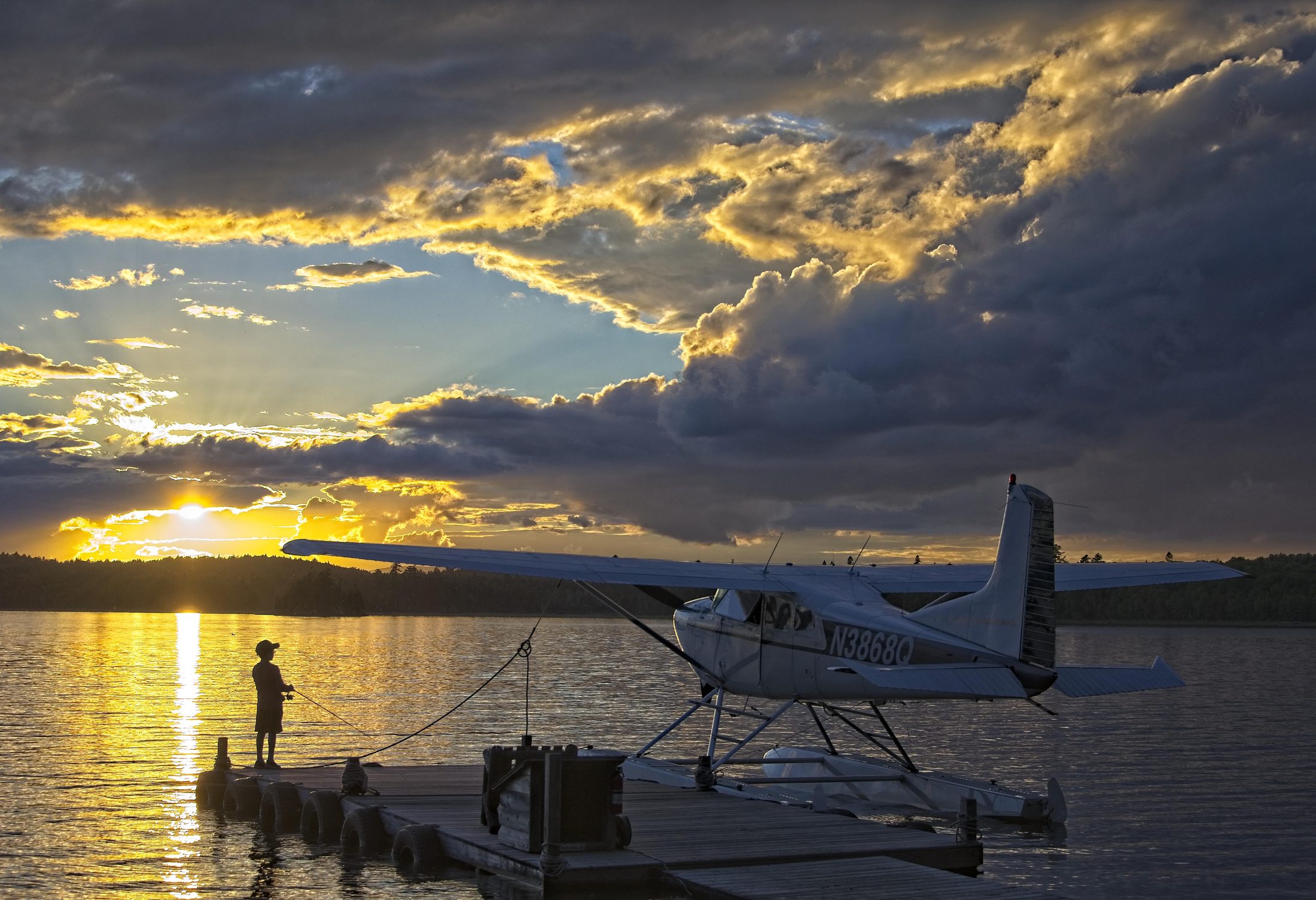 Seaplane at sunset, boy fishing from dock