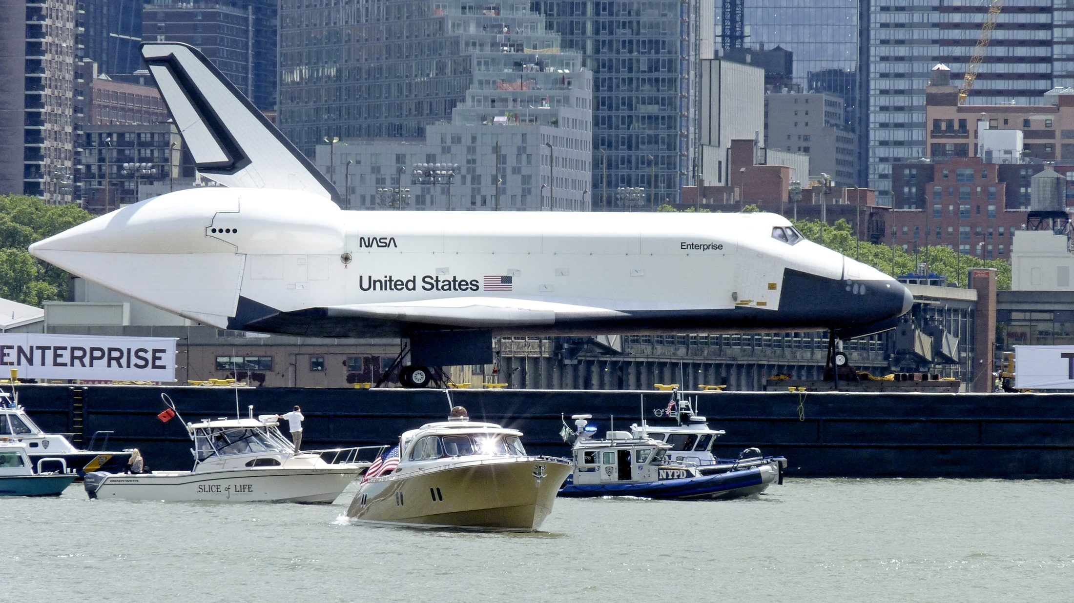 Space Shuttle Enterprise on transport barge, small boats alongside